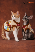 Two cats wearing the CatMellow cream teddy bear bow tie sleeveless knit sweater in a natural studio pose