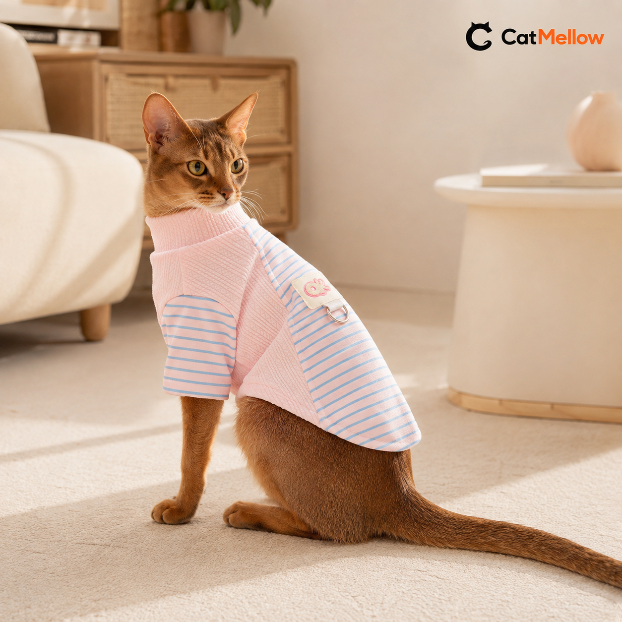 Cat wearing the pink CatMellow pastel stripe knit shirt in a warm home.