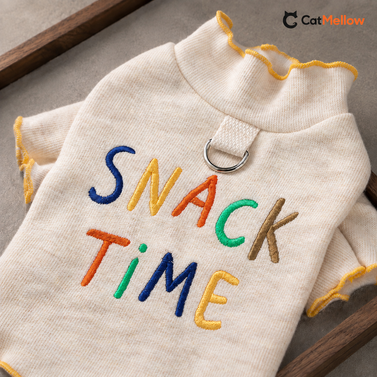 Close-up of multicolor SNACK TIME embroidery, cream polyester fabric and the metal D-ring on the cat T-shirt