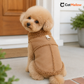 Apricot toy poodle wearing a brown sherpa-trim dog vest on a house porch.